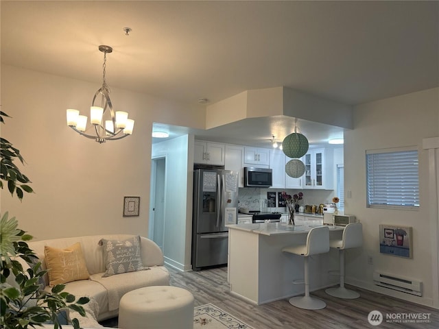 kitchen with glass insert cabinets, appliances with stainless steel finishes, a peninsula, white cabinets, and a baseboard radiator