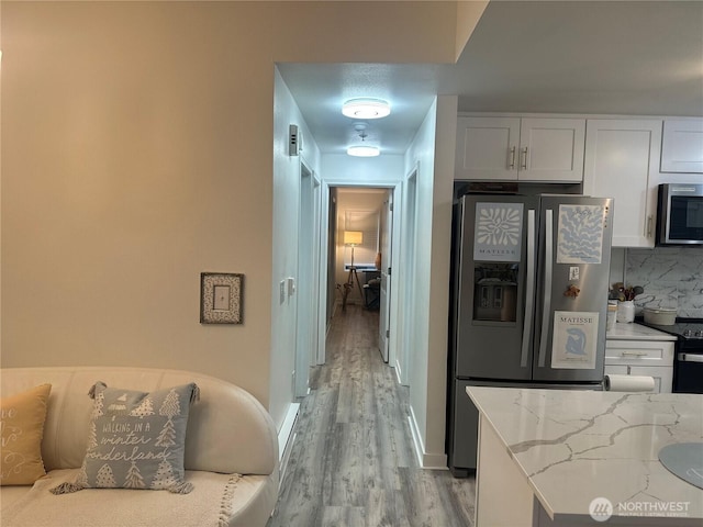 kitchen with tasteful backsplash, light stone counters, light wood-style floors, white cabinets, and stainless steel appliances