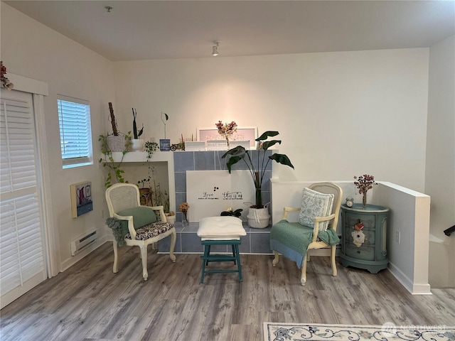 sitting room with a baseboard heating unit, wood finished floors, and baseboards