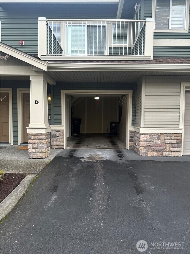 exterior space with a garage, stone siding, a balcony, and driveway