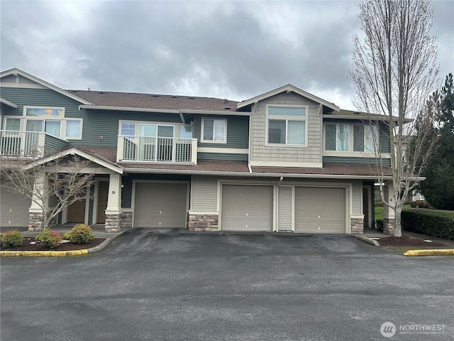 view of property with stone siding, driveway, an attached garage, and a balcony