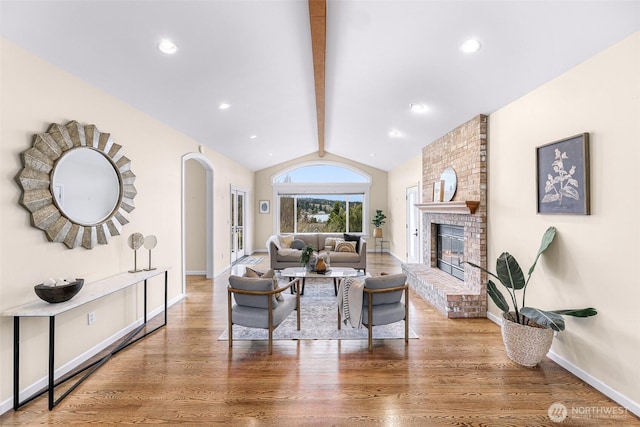 living area with baseboards, lofted ceiling with beams, a fireplace, wood finished floors, and arched walkways