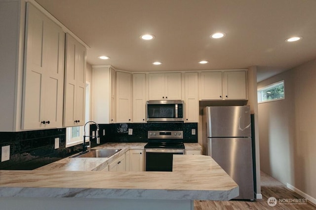 kitchen featuring stainless steel appliances, light countertops, decorative backsplash, white cabinetry, and a sink