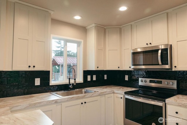 kitchen with stainless steel appliances, white cabinets, a sink, and backsplash