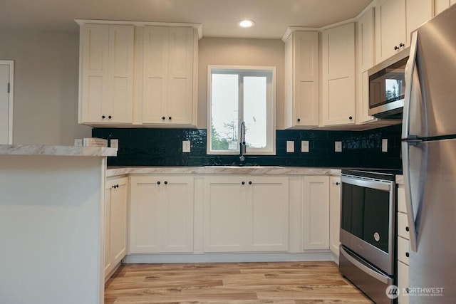 kitchen with light wood-type flooring, appliances with stainless steel finishes, white cabinets, and backsplash