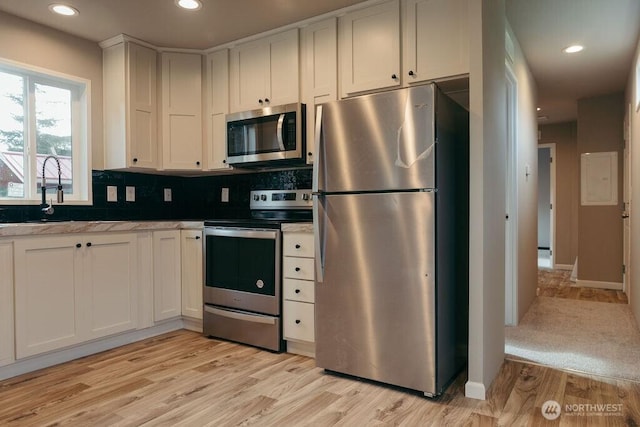 kitchen with a sink, light wood-style floors, white cabinets, appliances with stainless steel finishes, and tasteful backsplash