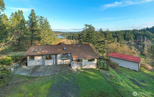 view of front of home featuring a patio area, a tiled roof, a front yard, and a view of trees