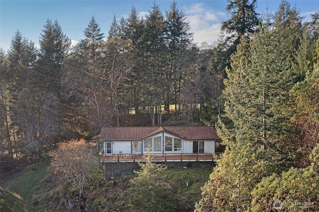 exterior space featuring a tiled roof, a wooden deck, and a view of trees