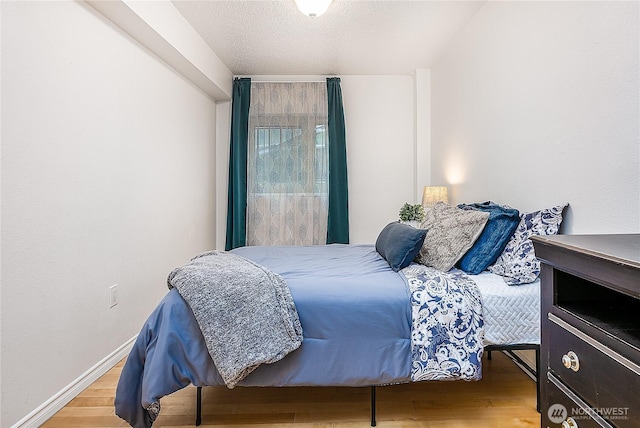 bedroom with a textured ceiling, wood finished floors, and baseboards