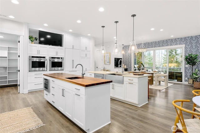 kitchen with pendant lighting, stainless steel appliances, wooden counters, a kitchen island with sink, and a sink