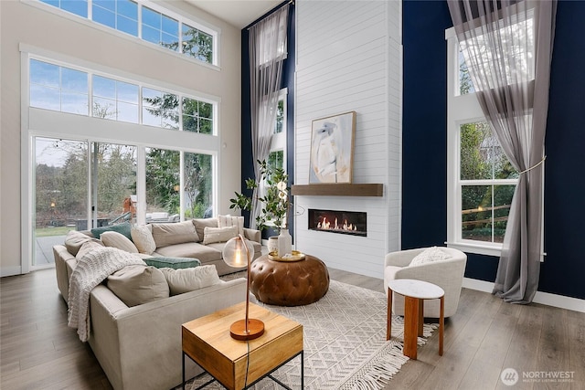 living room with a large fireplace, wood finished floors, a towering ceiling, and baseboards