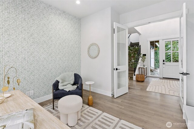 sitting room with recessed lighting, an accent wall, baseboards, light wood-style floors, and french doors