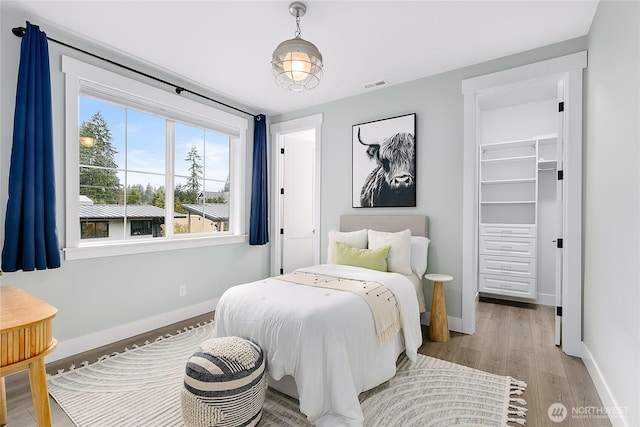 bedroom featuring light wood finished floors, baseboards, visible vents, and a walk in closet