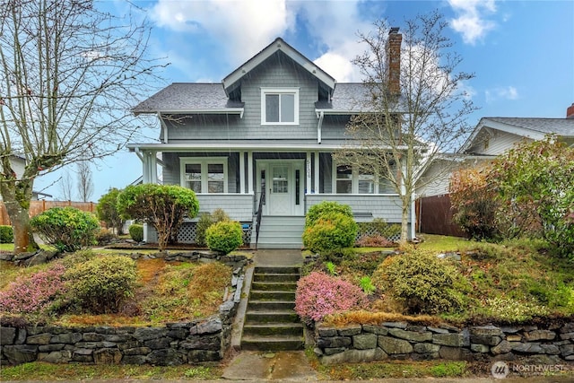 view of front of house with a shingled roof, covered porch, fence, and a chimney