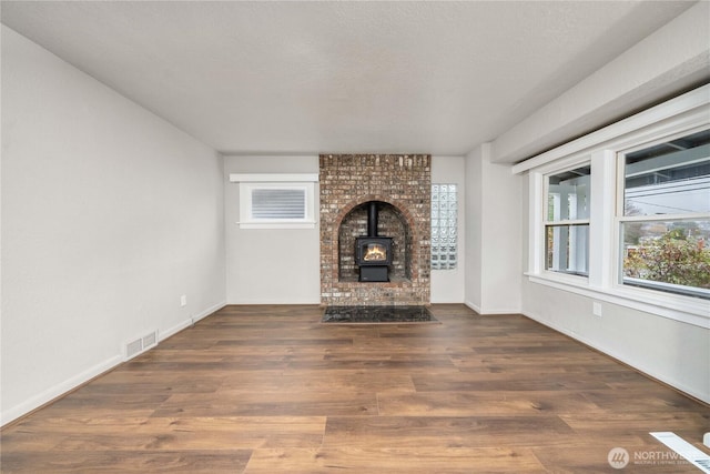 unfurnished living room featuring baseboards, visible vents, dark wood-style floors, a wood stove, and a textured ceiling