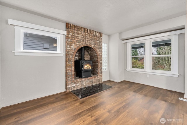 unfurnished living room with a textured ceiling, dark wood finished floors, a wood stove, and baseboards