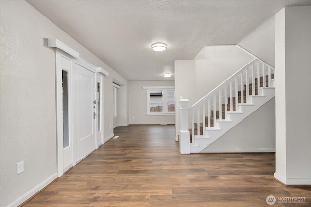 foyer featuring a textured ceiling, stairway, dark wood-style flooring, and baseboards