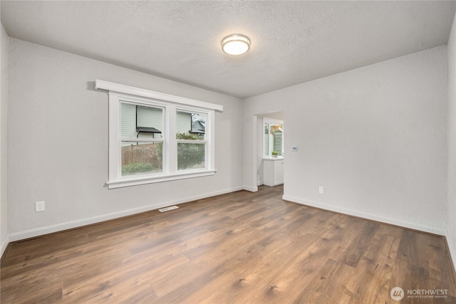 spare room with a textured ceiling, dark wood-style flooring, and baseboards