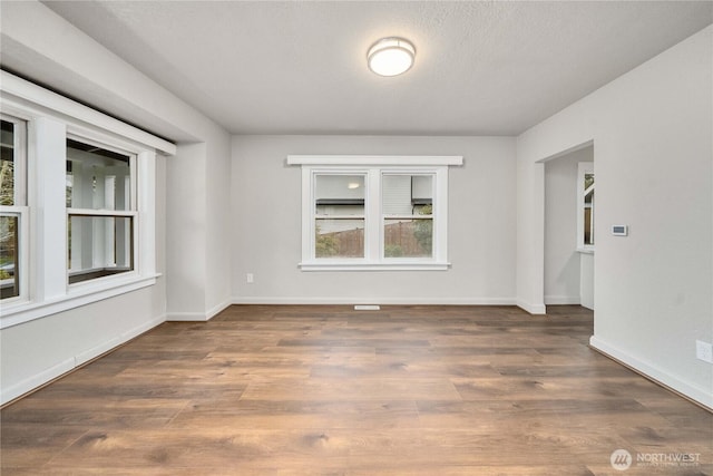 unfurnished room with dark wood-style floors, a textured ceiling, and baseboards