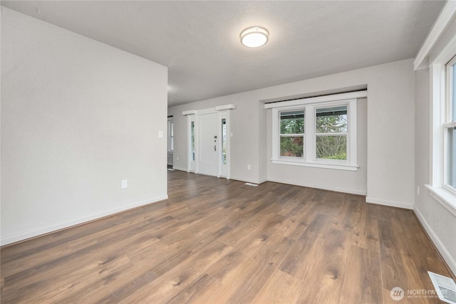 empty room featuring dark wood-style flooring, visible vents, a textured ceiling, and baseboards