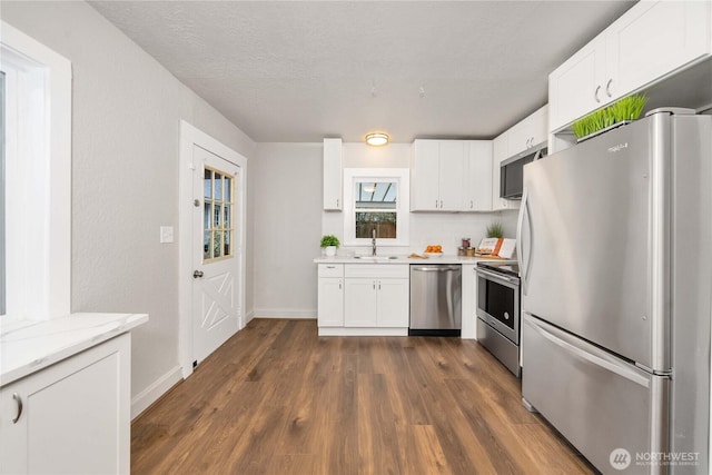 kitchen with dark wood-style flooring, appliances with stainless steel finishes, white cabinets, and a sink