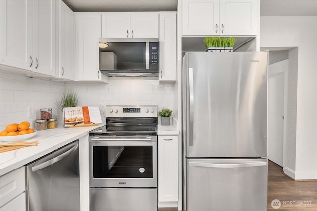 kitchen featuring appliances with stainless steel finishes, white cabinets, backsplash, and light stone counters