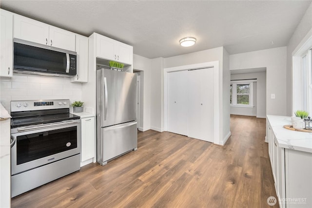 kitchen featuring dark wood-style floors, appliances with stainless steel finishes, backsplash, and white cabinetry