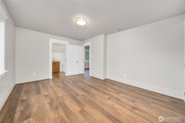 unfurnished bedroom featuring baseboards, visible vents, connected bathroom, wood finished floors, and a textured ceiling