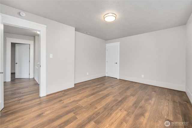 empty room with dark wood-style floors, visible vents, a textured ceiling, and baseboards