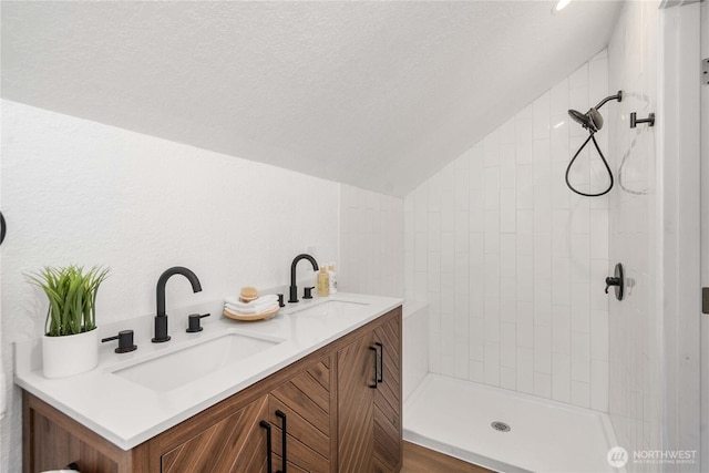 full bath featuring lofted ceiling, double vanity, a textured ceiling, and a sink