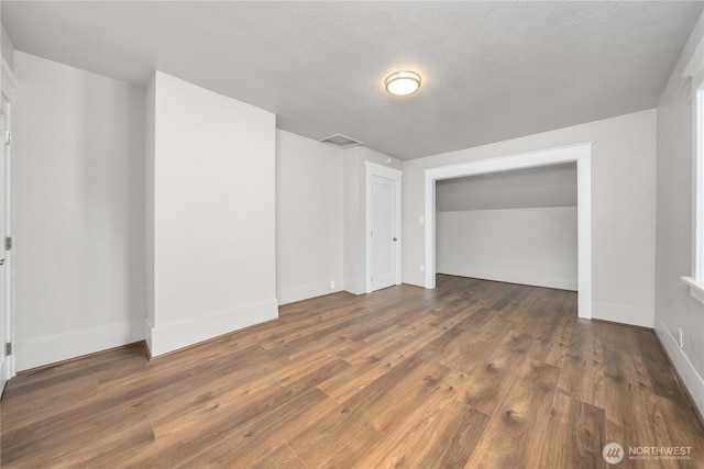 interior space with a textured ceiling, baseboards, and dark wood-type flooring