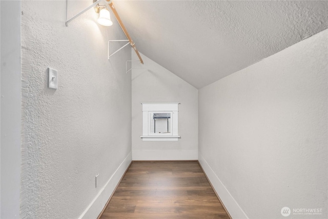 additional living space with dark wood finished floors, a textured wall, vaulted ceiling, a textured ceiling, and baseboards