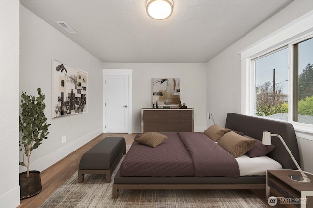 bedroom with wood finished floors, visible vents, and baseboards