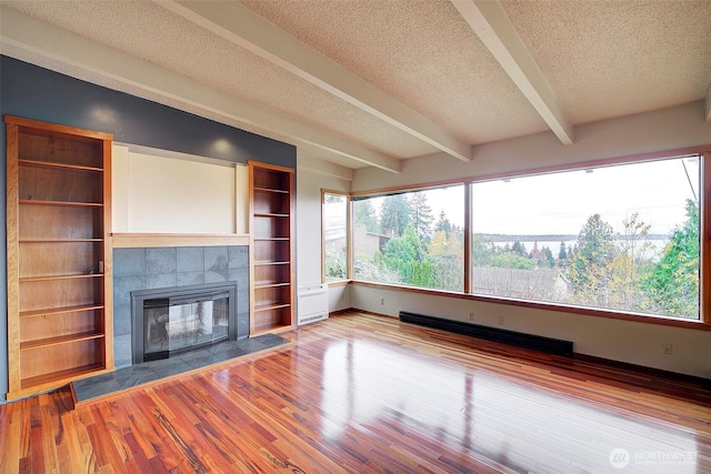 unfurnished living room with a tiled fireplace, beamed ceiling, wood finished floors, a textured ceiling, and a baseboard heating unit