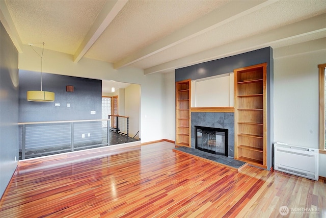 unfurnished living room featuring a tiled fireplace, wood finished floors, heating unit, a textured ceiling, and beam ceiling