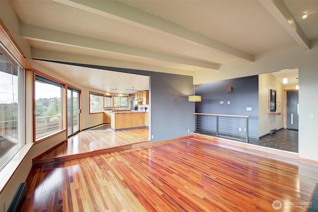 unfurnished living room with baseboards, a textured ceiling, beam ceiling, and light wood-style floors