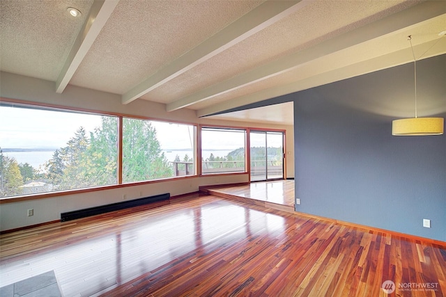 unfurnished room featuring baseboard heating, a textured ceiling, wood finished floors, beamed ceiling, and baseboards