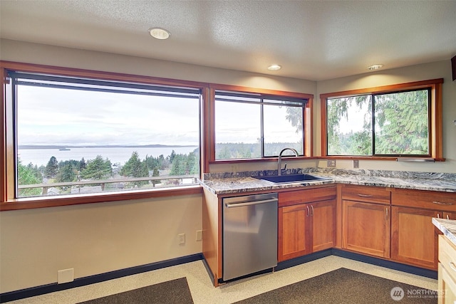 kitchen featuring baseboards, brown cabinetry, light stone counters, a sink, and stainless steel dishwasher