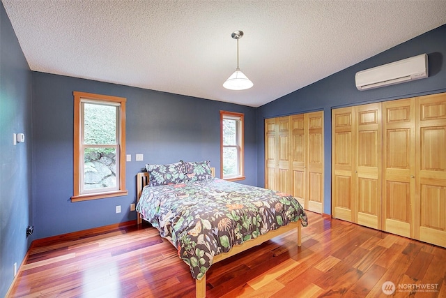 bedroom with baseboards, lofted ceiling, wood finished floors, an AC wall unit, and multiple closets