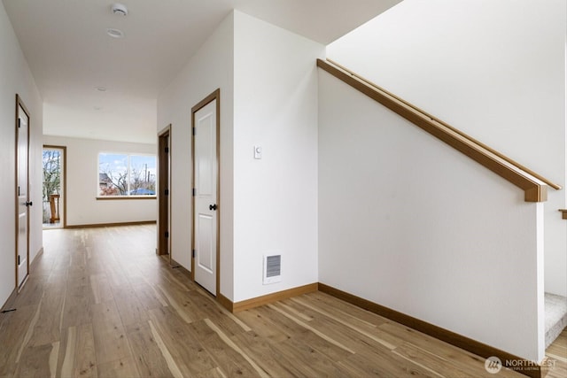 hallway featuring light wood finished floors, baseboards, and visible vents