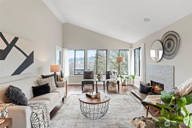 living area with plenty of natural light, a fireplace, high vaulted ceiling, and wood finished floors