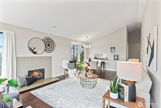 living room featuring lofted ceiling, a brick fireplace, baseboards, and wood finished floors