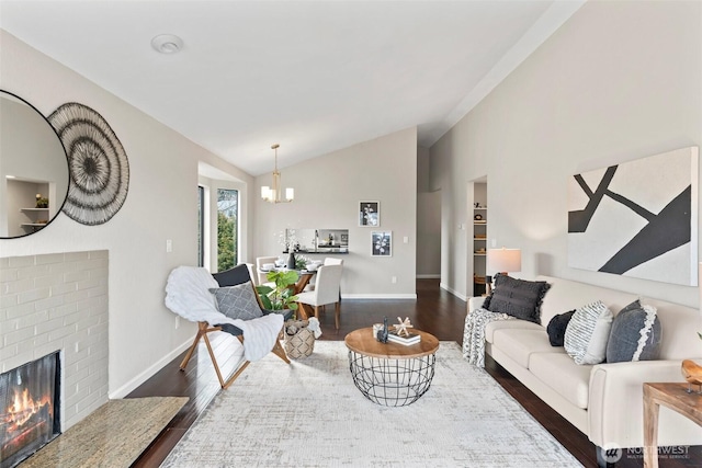 living area with baseboards, lofted ceiling, dark wood-style floors, a brick fireplace, and a chandelier