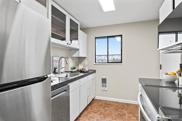 kitchen with a sink, white cabinets, appliances with stainless steel finishes, dark countertops, and glass insert cabinets