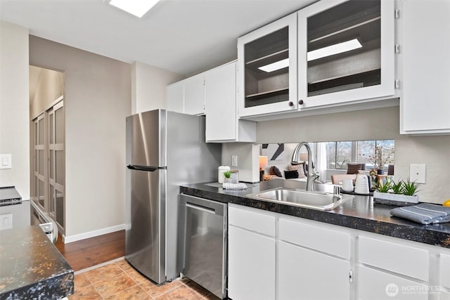 kitchen with appliances with stainless steel finishes, glass insert cabinets, white cabinets, a sink, and baseboards