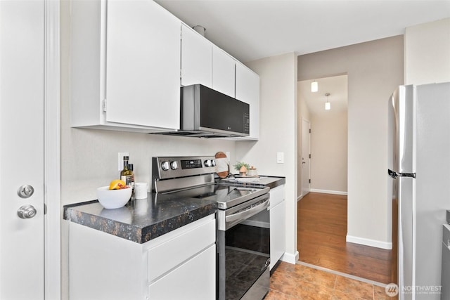 kitchen with stainless steel appliances, dark countertops, white cabinets, light tile patterned flooring, and baseboards