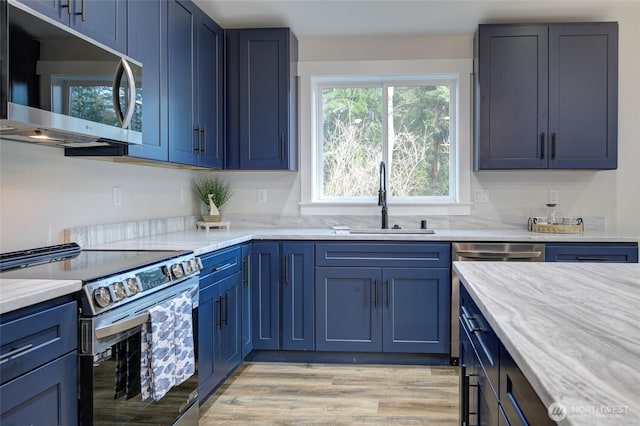 kitchen with stainless steel appliances, blue cabinetry, a sink, and light wood-style flooring