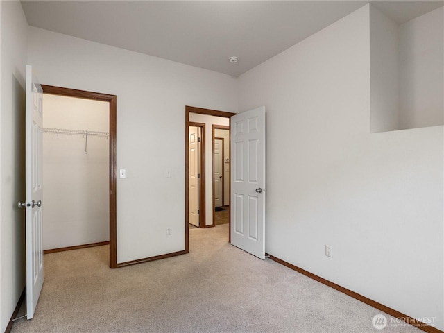 unfurnished bedroom featuring a walk in closet, a closet, light carpet, and baseboards