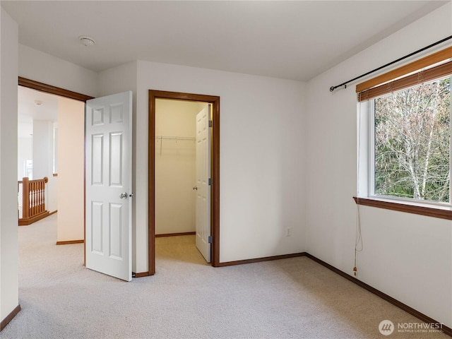 unfurnished bedroom featuring light carpet, baseboards, a walk in closet, and a closet