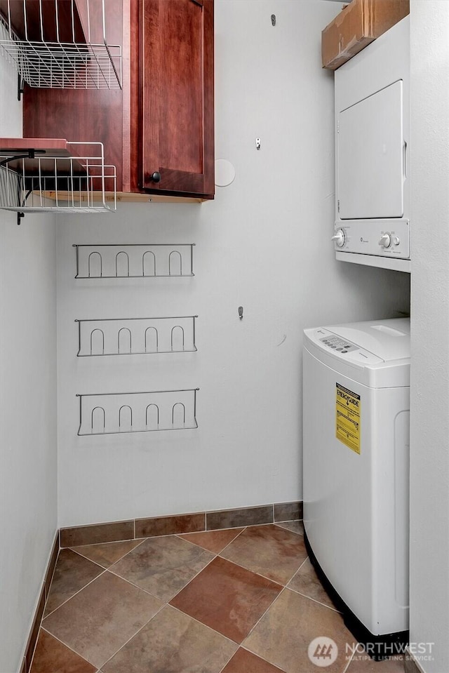 laundry room featuring tile patterned floors, cabinet space, stacked washer and clothes dryer, and baseboards